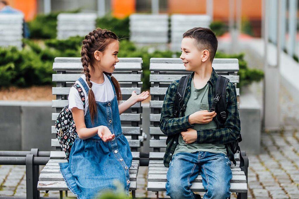 two children having a conversation on a bench demonstrating how to help children with autism make friends